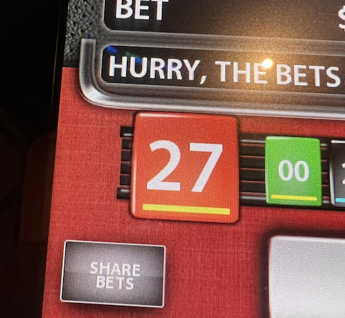 A digital display screen showing a casino betting interface, with text prompting to hurry bets and a highlighted number 27 in red. There are options for betting amounts and a 'share bets' button.
